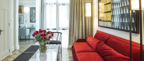 A modern living room with a red sofa, a glass coffee table with a vase of flowers, and a dining area in the background.