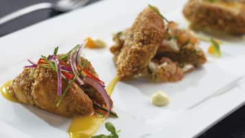 Une assiette blanche contenant deux morceaux de poulet pané, garnis d’oignons rouges et d’herbes, et une cuillerée de sauce.
