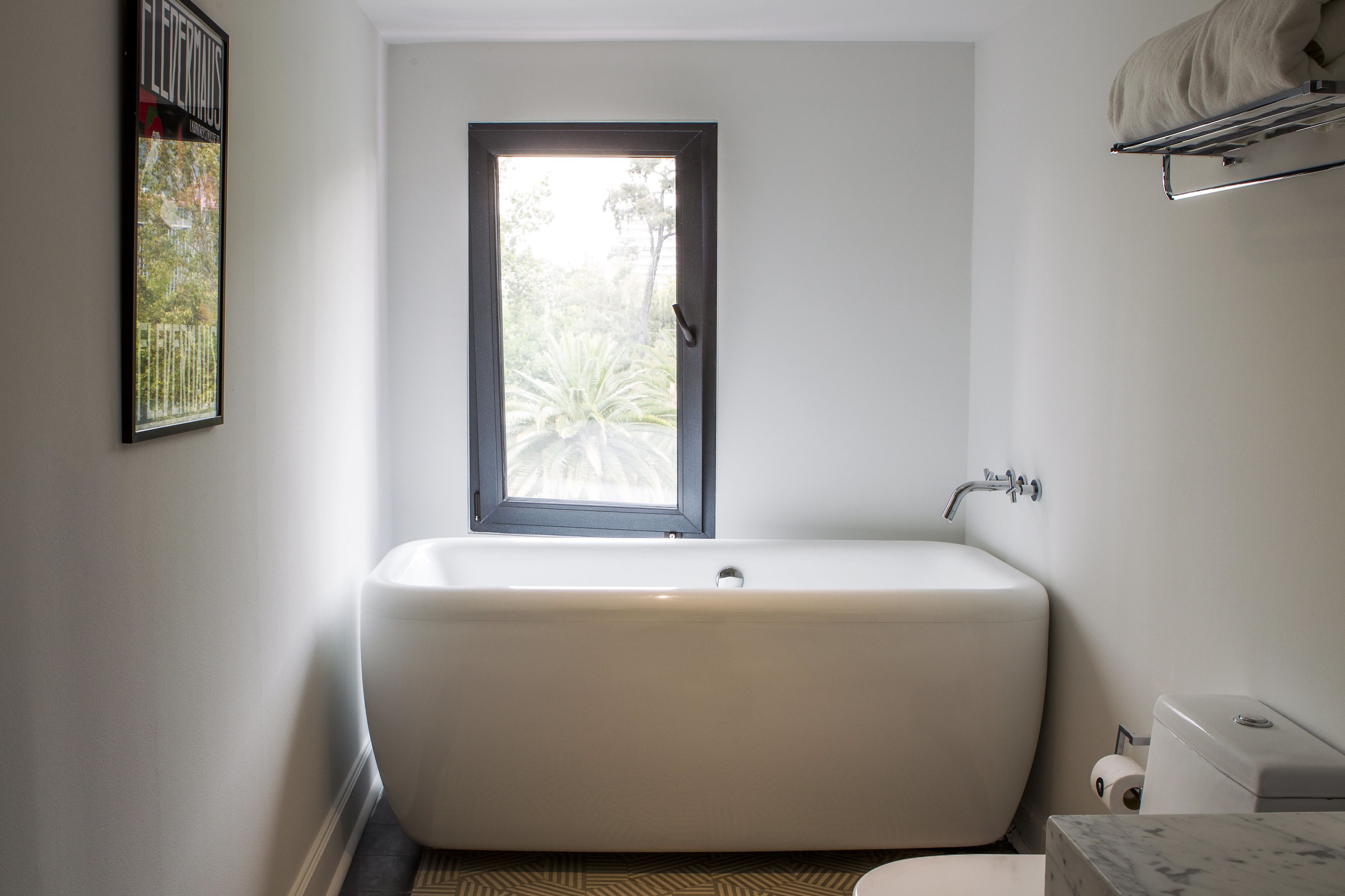 A modern bathroom with a freestanding bathtub, a toilet, and a window providing natural light.