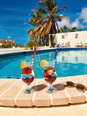 Two cocktails with lime slices and straws by a pool with palm trees and lounge chairs in the background. - Karibu Aruba Boutique Hotel (Noord)