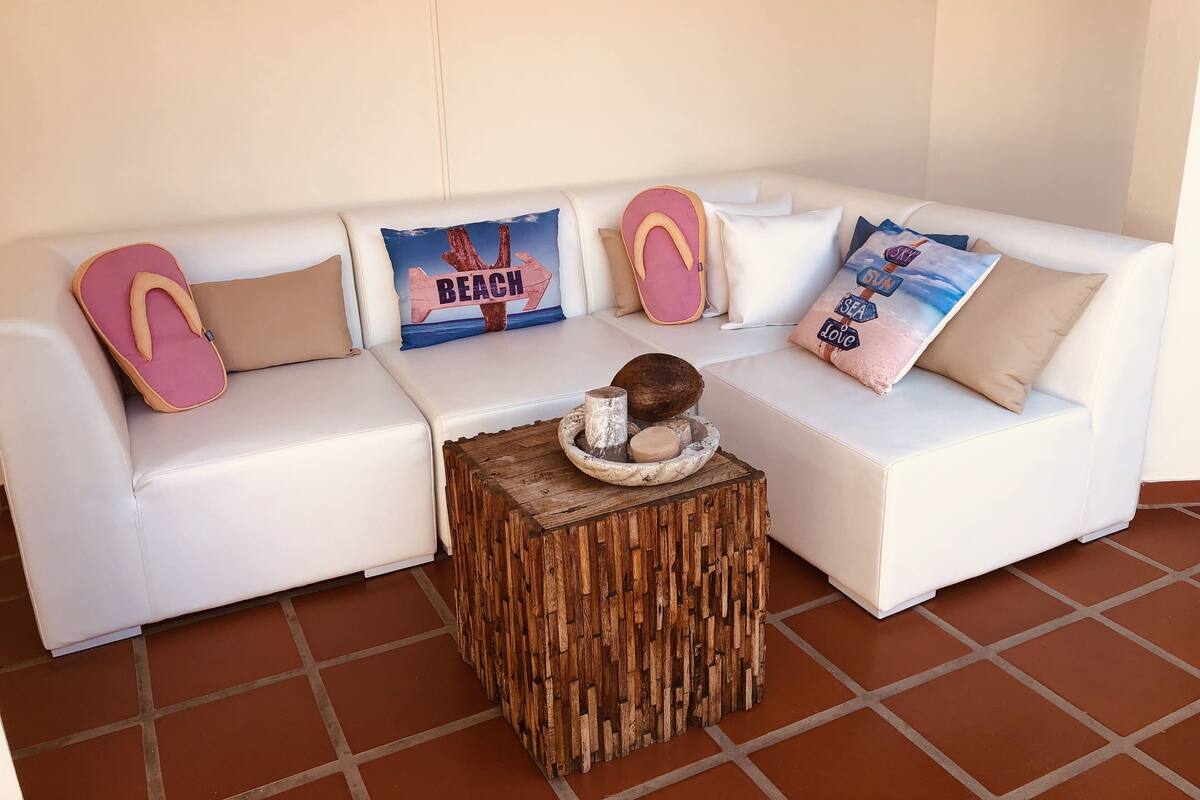 A white sectional sofa with beach-themed pillows and a rustic wooden side table with a decorative bowl.