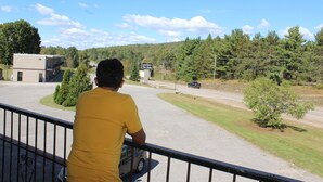 A man in a yellow shirt standing on a balcony overlooking a road with a sign for a bank and a building in the background.