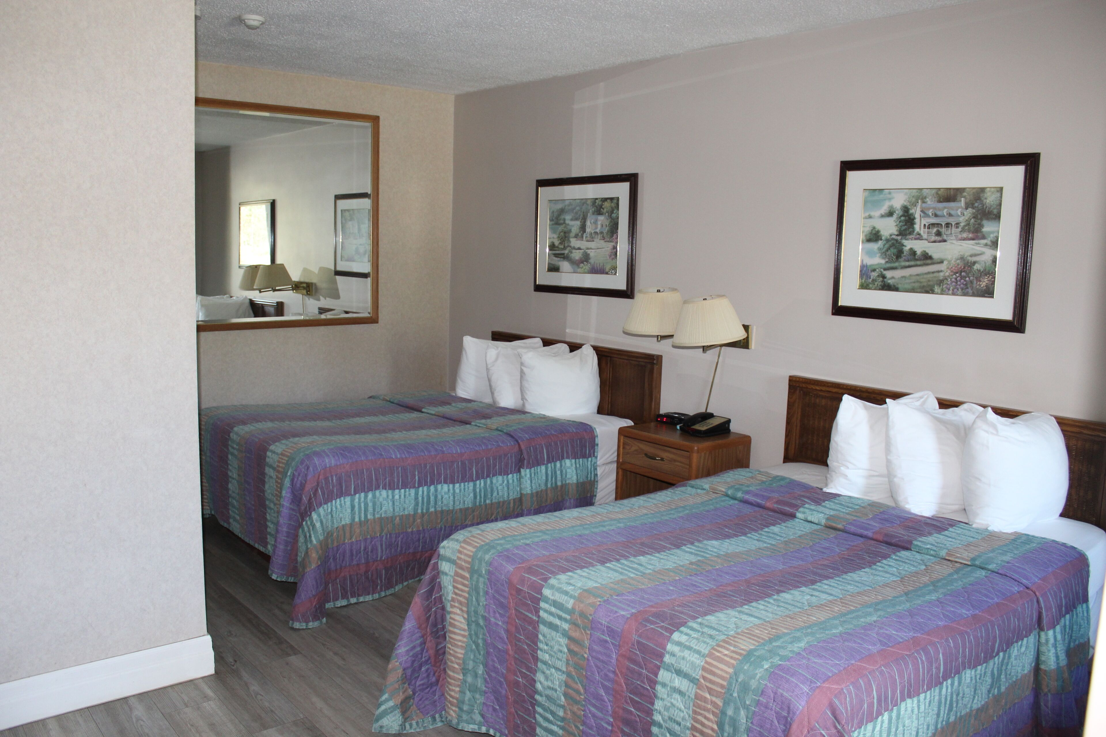 A hotel room with two beds, each with a striped bedspread, a nightstand with a lamp, and framed pictures on the wall.