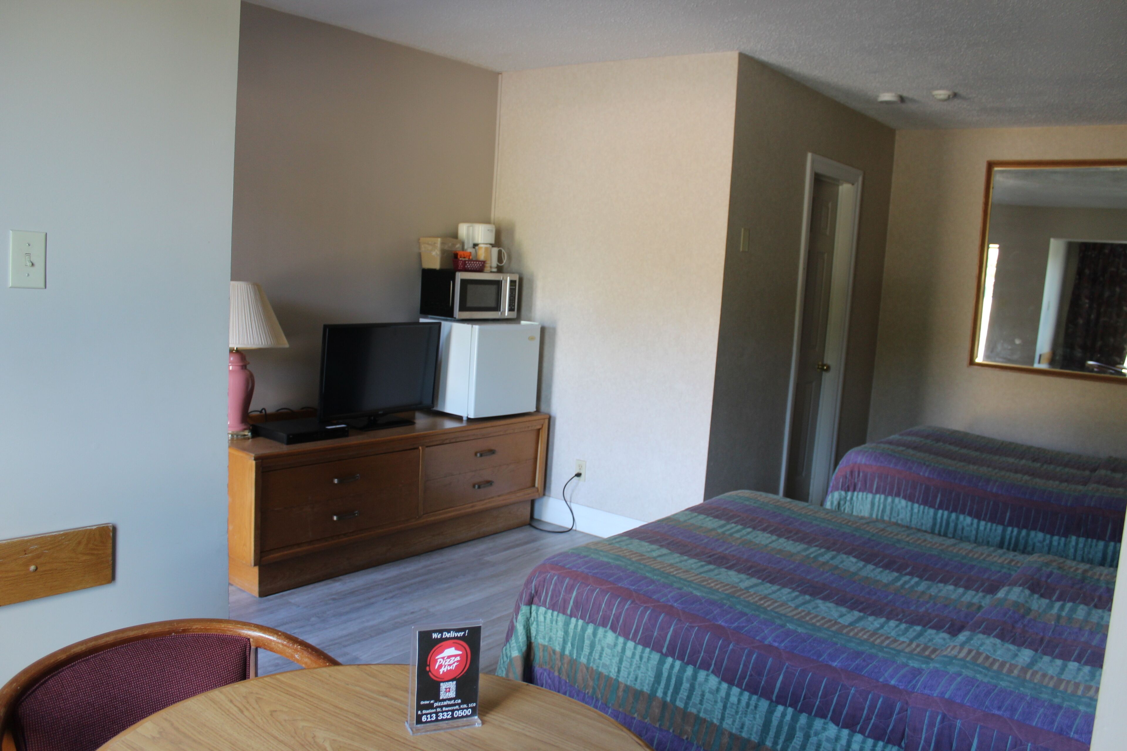 A hotel room with a bed, a television on a wooden dresser, a microwave, and a table with a sign.