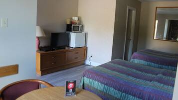 Habitación de hotel con cama, televisor sobre un aparador de madera, microondas y una mesa con un cartel.