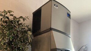 A stainless steel water dispenser with a water fountain feature, located in a corner of a room with a white brick wall and a wooden railing.