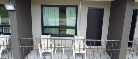 A balcony with a table and chairs, a window with curtains, and a door.