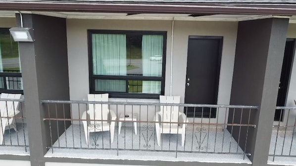 A balcony with a table and chairs, a window with curtains, and a door.