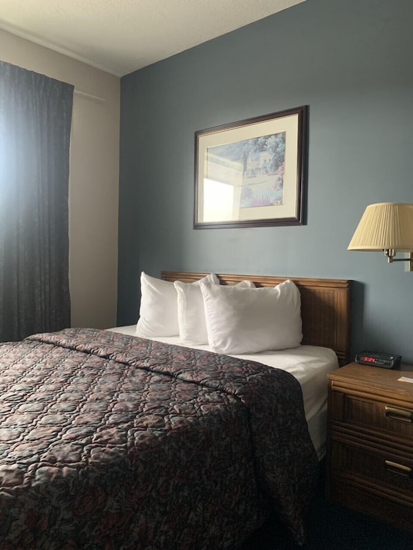 A hotel room with a bed, a nightstand, a lamp, and a framed picture on the wall.