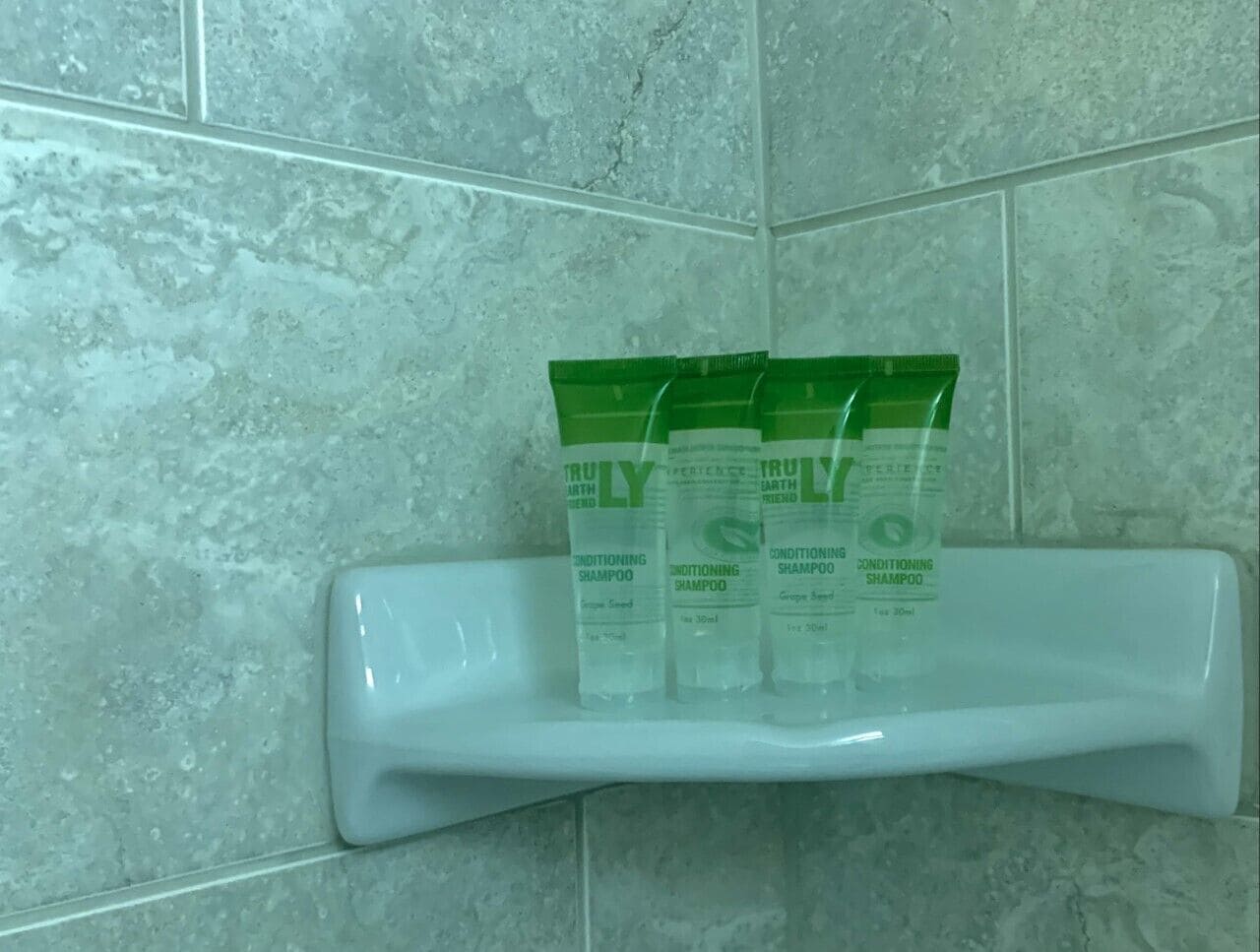 A bathroom shelf with three bottles of Truly Conditioning Shampoo.