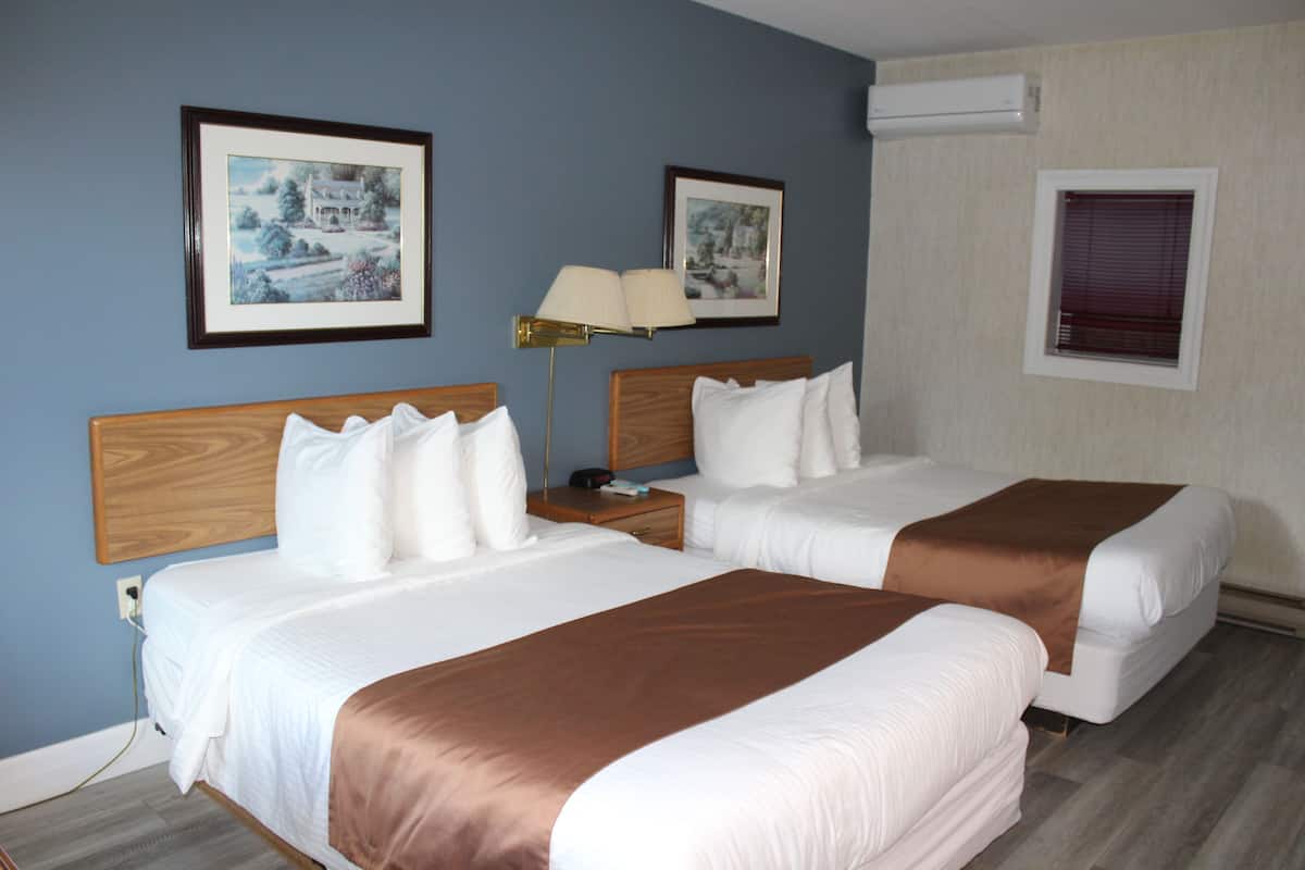 Ein Hotelzimmer mit zwei Betten, einem Nachttisch, einer Lampe und gerahmten Bildern an der Wand.