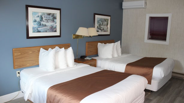 A hotel room with two beds, a nightstand, a lamp, and framed pictures on the wall.