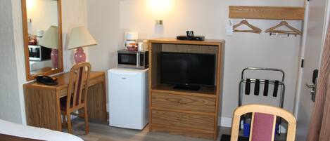Habitación de hotel compacta con cama, escritorio con lámpara, microondas, televisor y refrigerador pequeño.