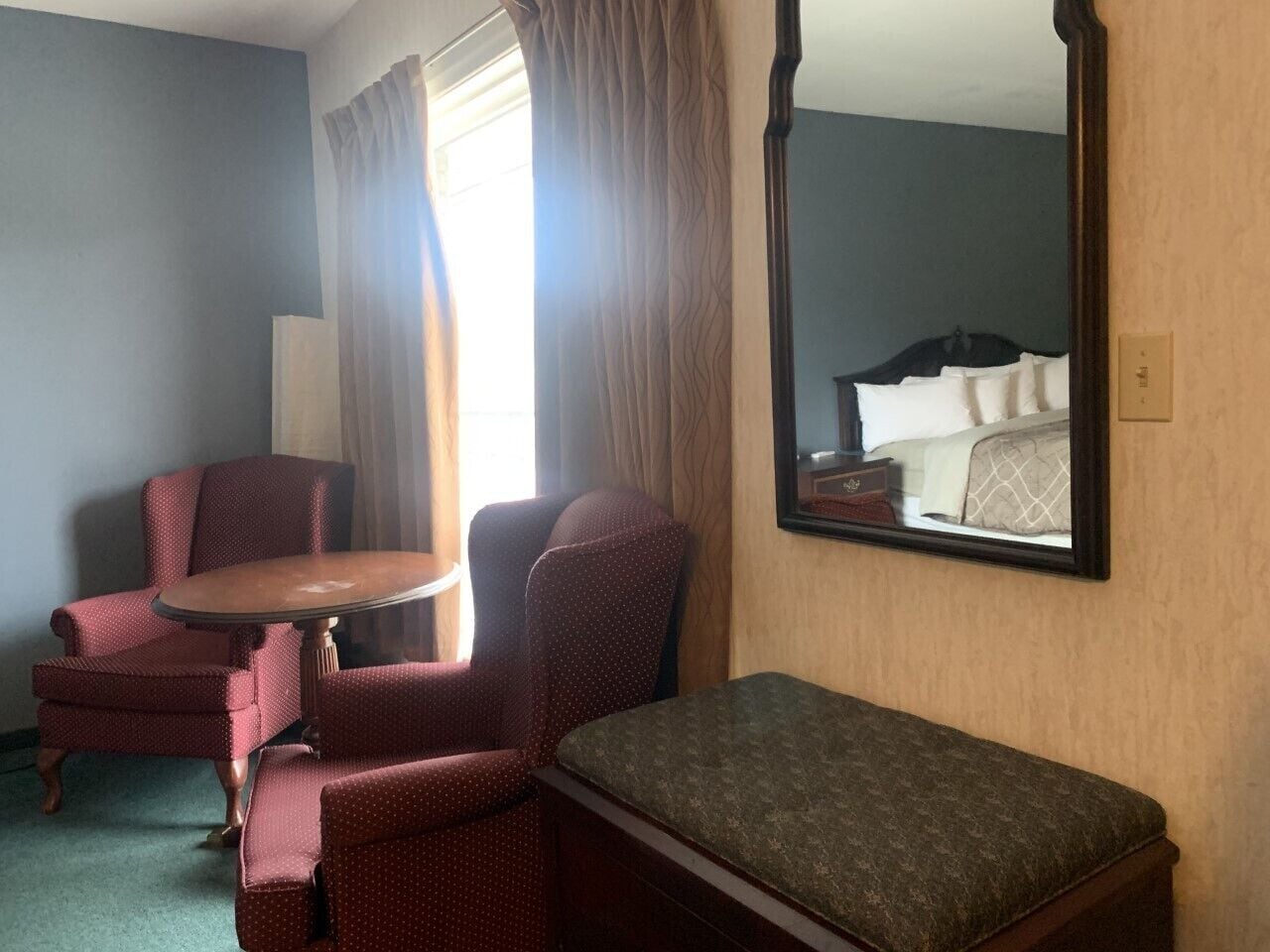 A hotel room with a bed, two armchairs, a small round table, and a large mirror.
