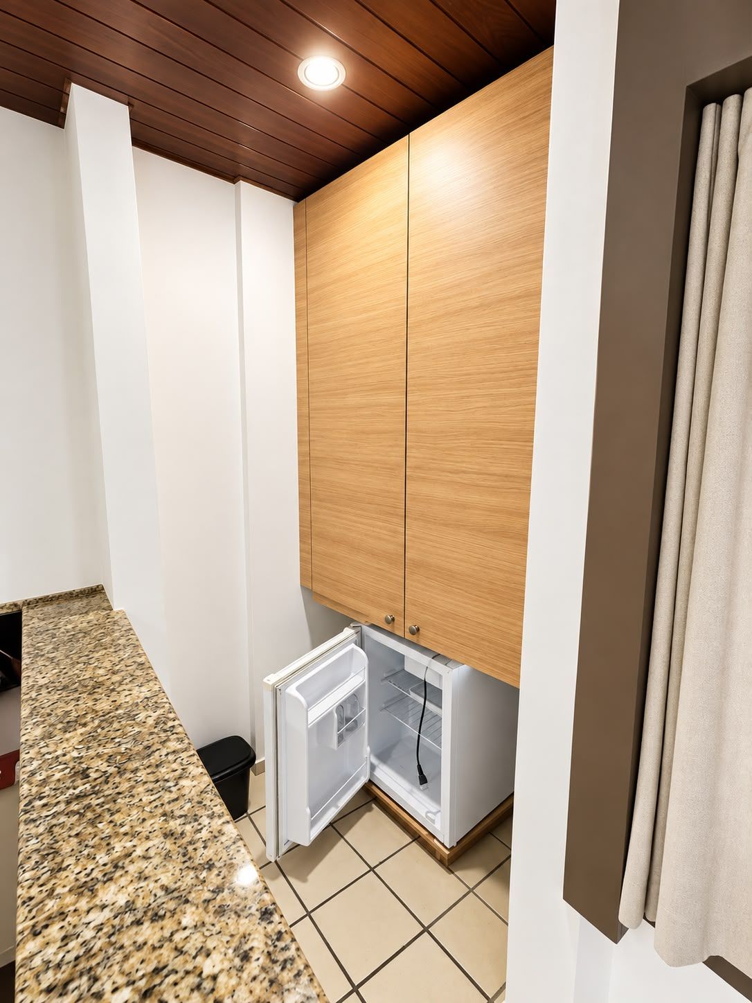 Una cucina compatta con frigorifero integrato, mobili in legno e piano di lavoro in granito.