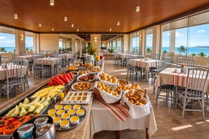 A buffet setup with various food items and a view of the ocean. - Xenius Hotel (João Pessoa)