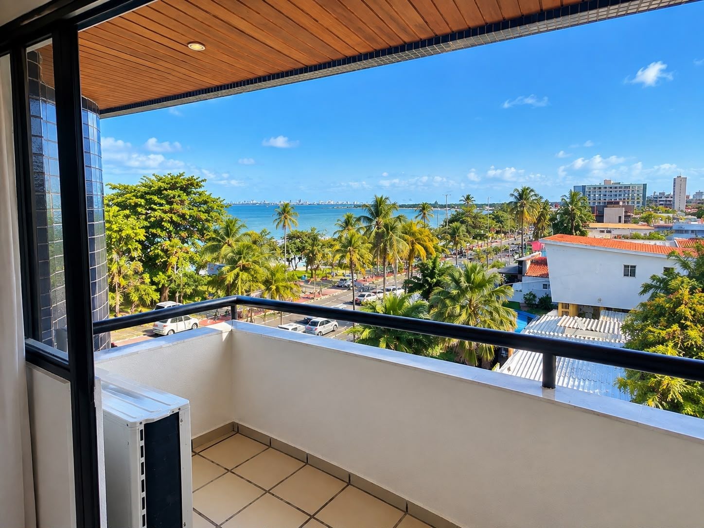 Uma varanda com vista para um horizonte costeiro, incluindo palmeiras e um céu azul límpido.