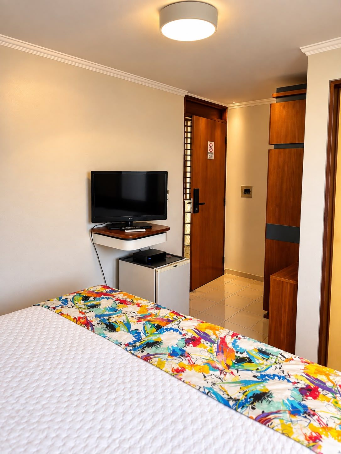 A hotel room with a bed, a television, a desk, and a door.