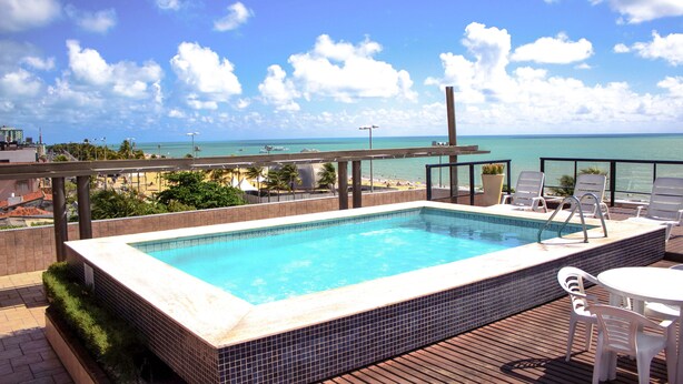 A rooftop pool with a view of the ocean, surrounded by lounge chairs and a table. - Xenius Hotel (João Pessoa)