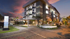 A modern hotel with multiple floors, a well-lit entrance, and a landscaped area with trees and plants. - Xenius Hotel (João Pessoa)