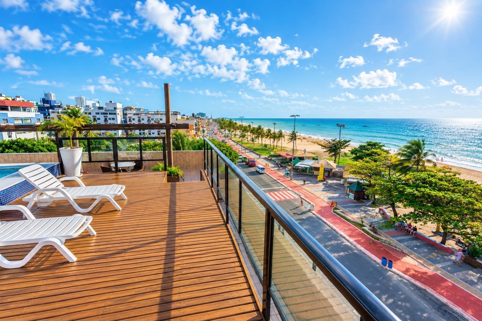 Varanda de madeira com cadeiras de descanso brancas com vista para uma praia e paisagem urbana.