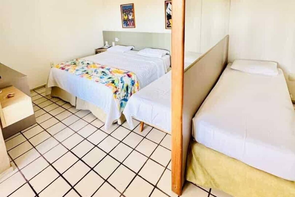 A room with two beds, one larger and one smaller, a wooden post in the center, and tiled flooring.