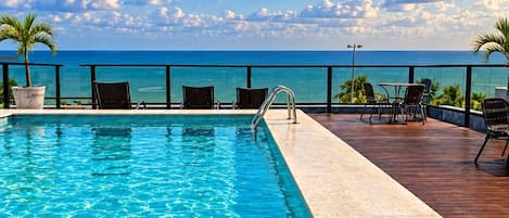 Une piscine avec vue sur l’océan, entourée de chaises longues et d’une terrasse en bois.