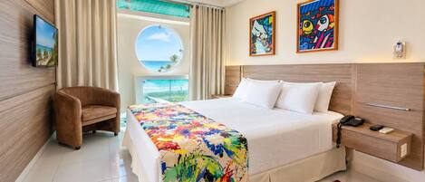 Una habitación de hotel con cama, una silla, un televisor, una ventana con cortinas y una obra de arte en la pared.