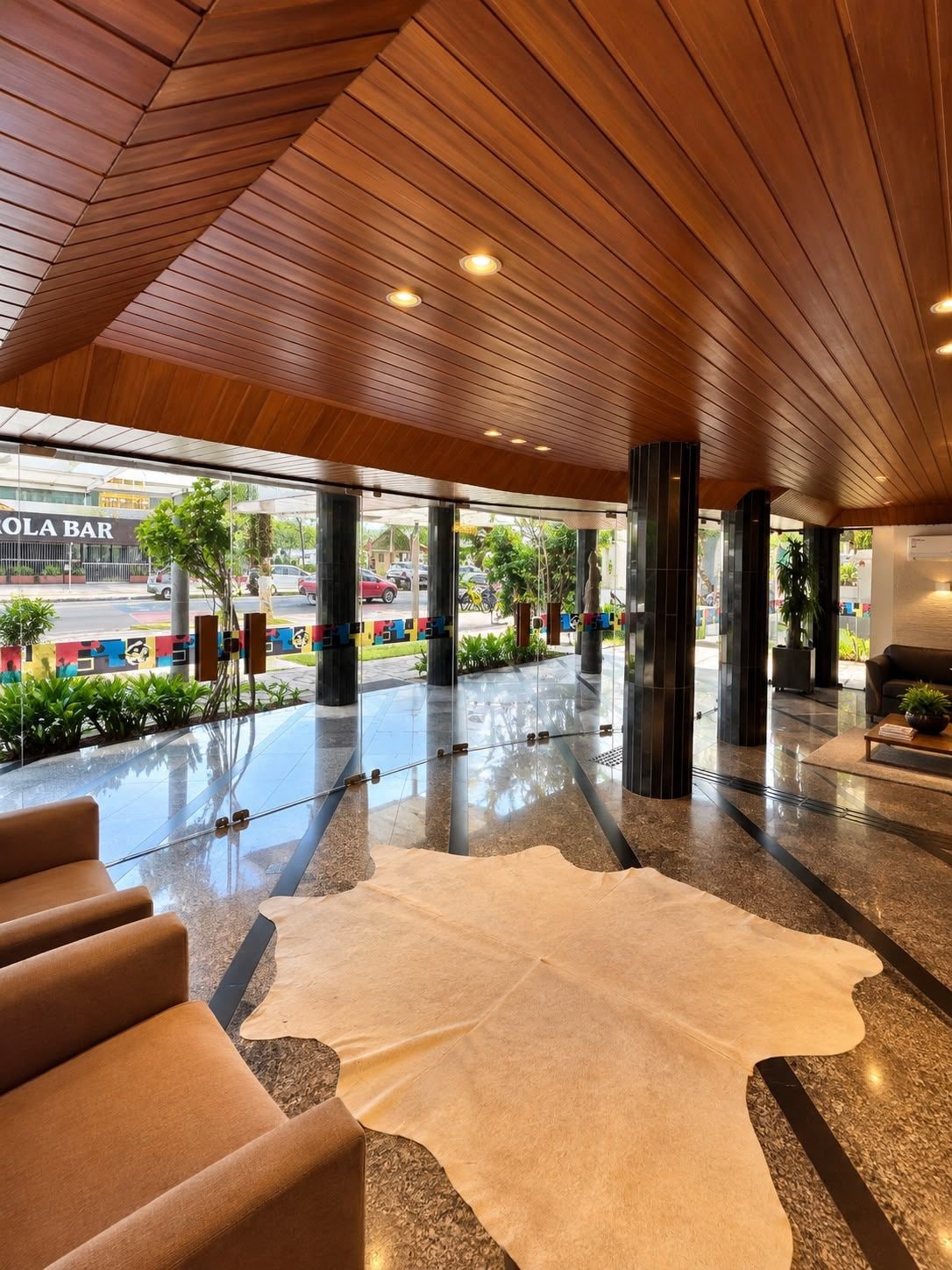 A modern lobby with a wooden ceiling, a glass entrance, and a seating area with a white rug.