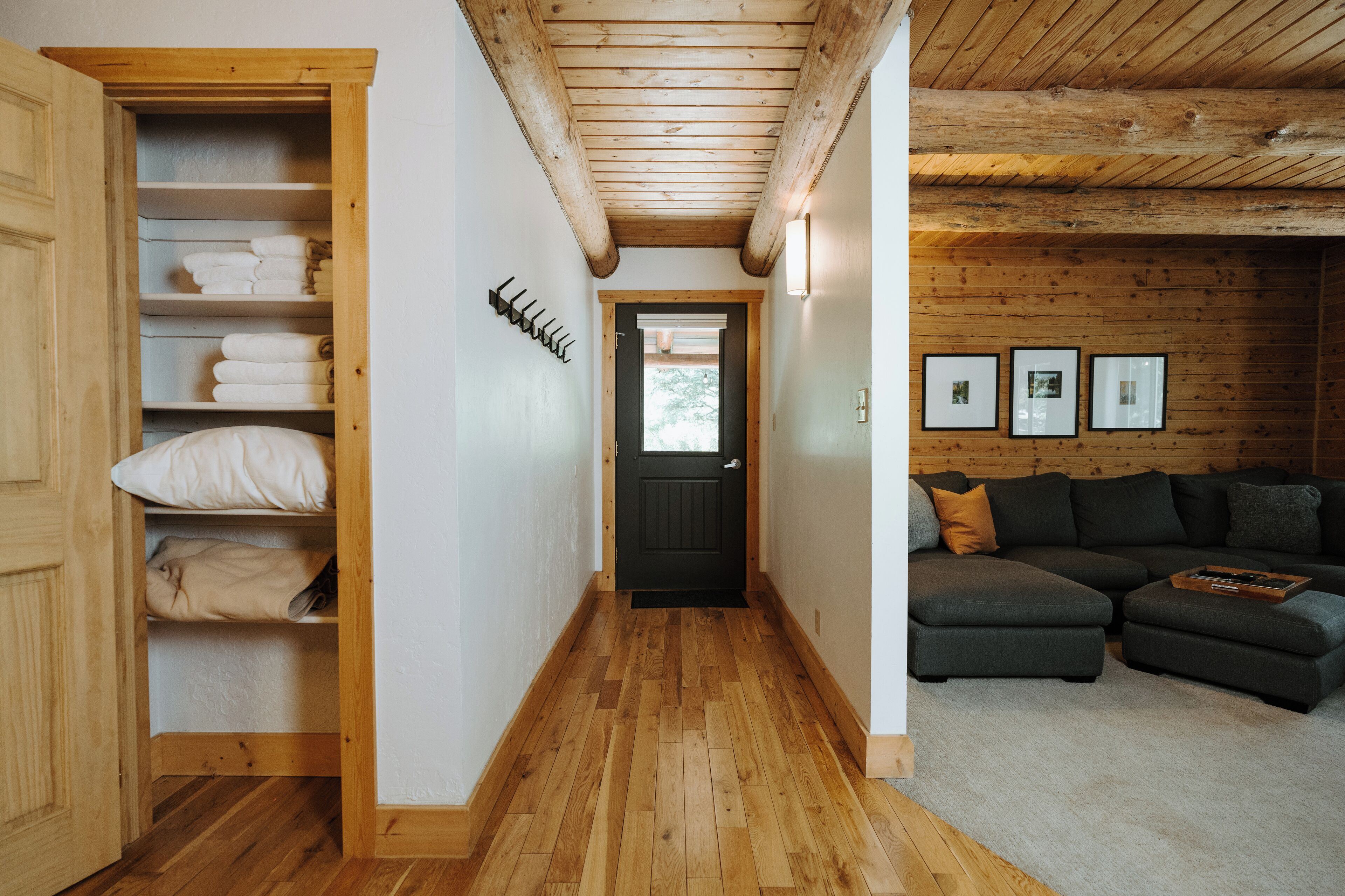 Een houten interieur met een hal die leidt naar een donkere deur, een zithoek met een hoekbank en een houten kast met opgevouwen handdoeken.