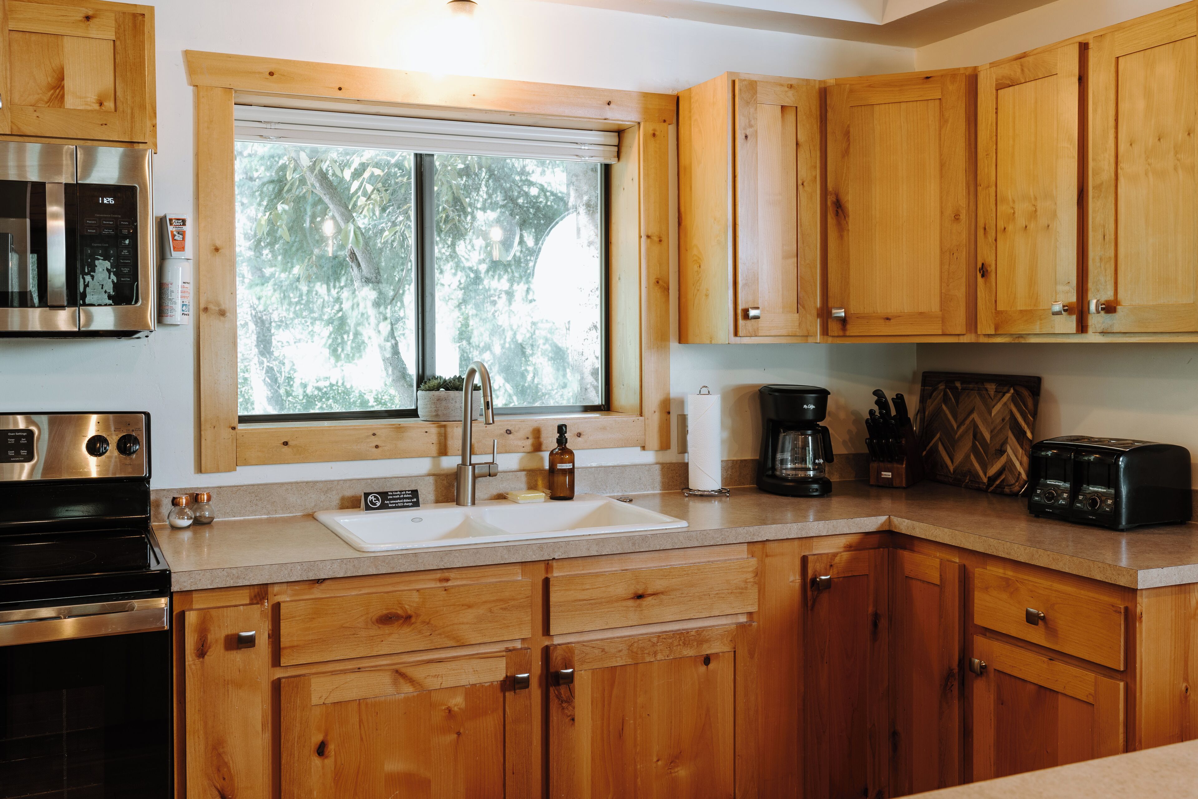 A modern kitchen with wooden cabinets, a stainless steel stove, a double sink, and a window providing natural light.