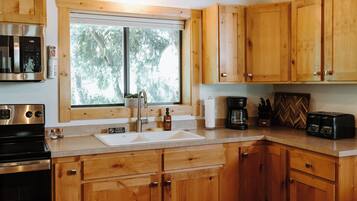 A modern kitchen with wooden cabinets, a stainless steel stove, a double sink, and a window providing natural light.