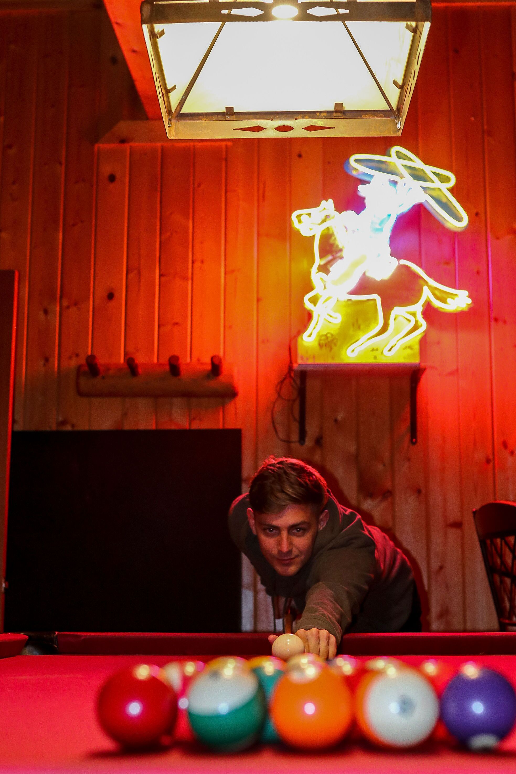 A pool table with a neon horse sign in the background.