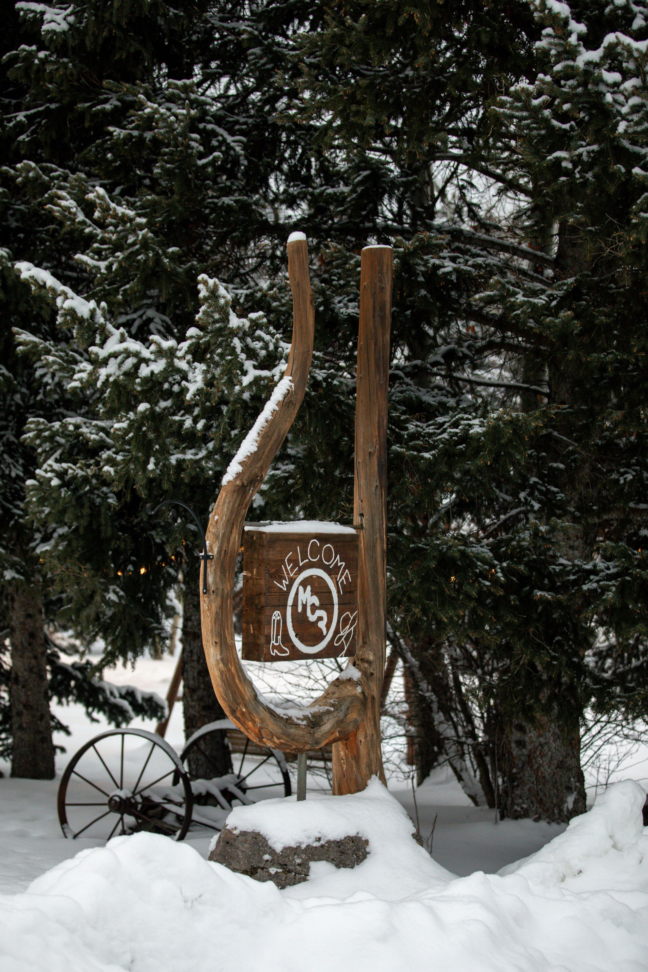 A wooden welcome sign with a snow-covered background and a bicycle wheel.