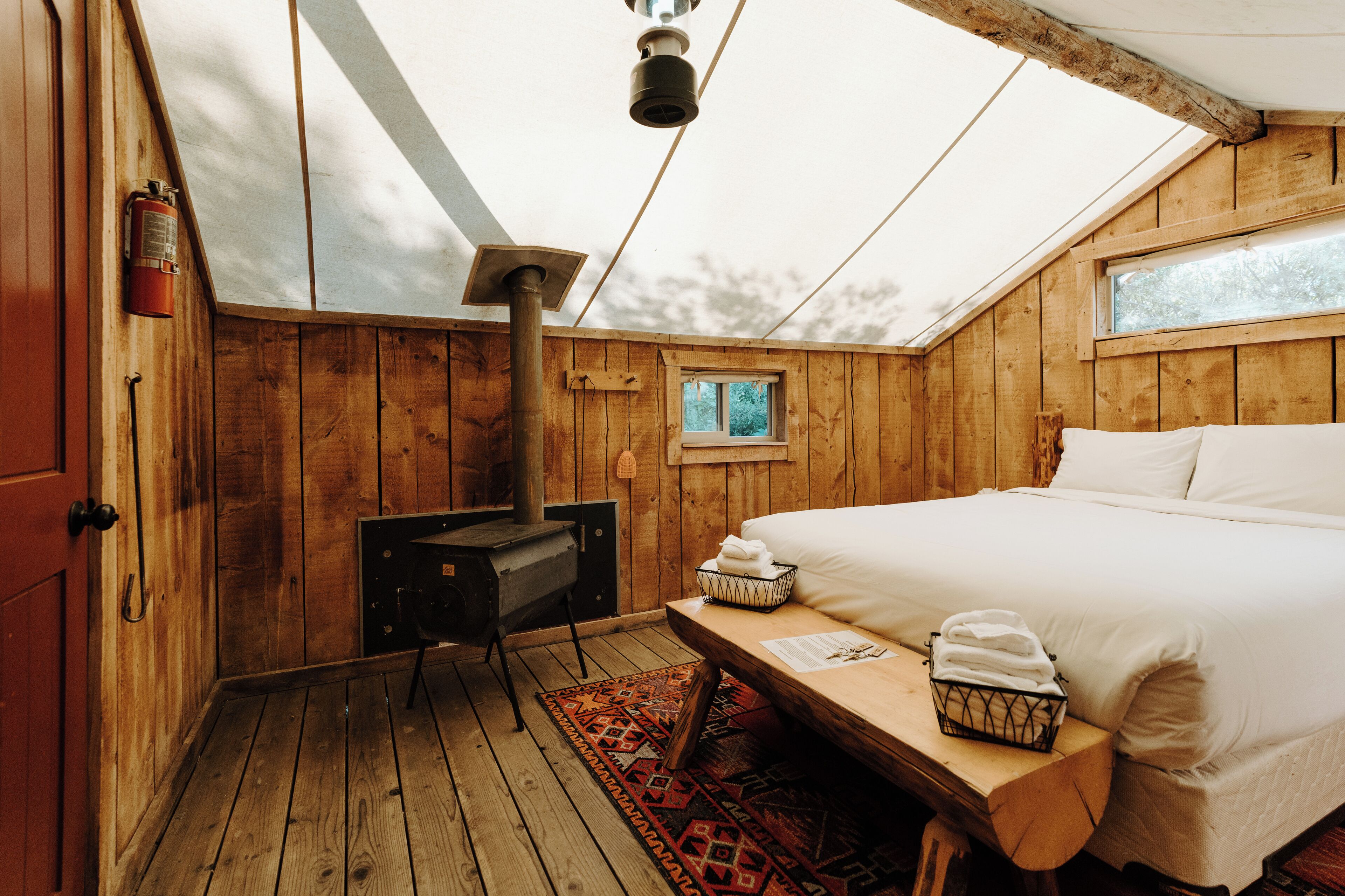 A wooden cabin bedroom with a bed, a heater, a window, and a fire extinguisher.