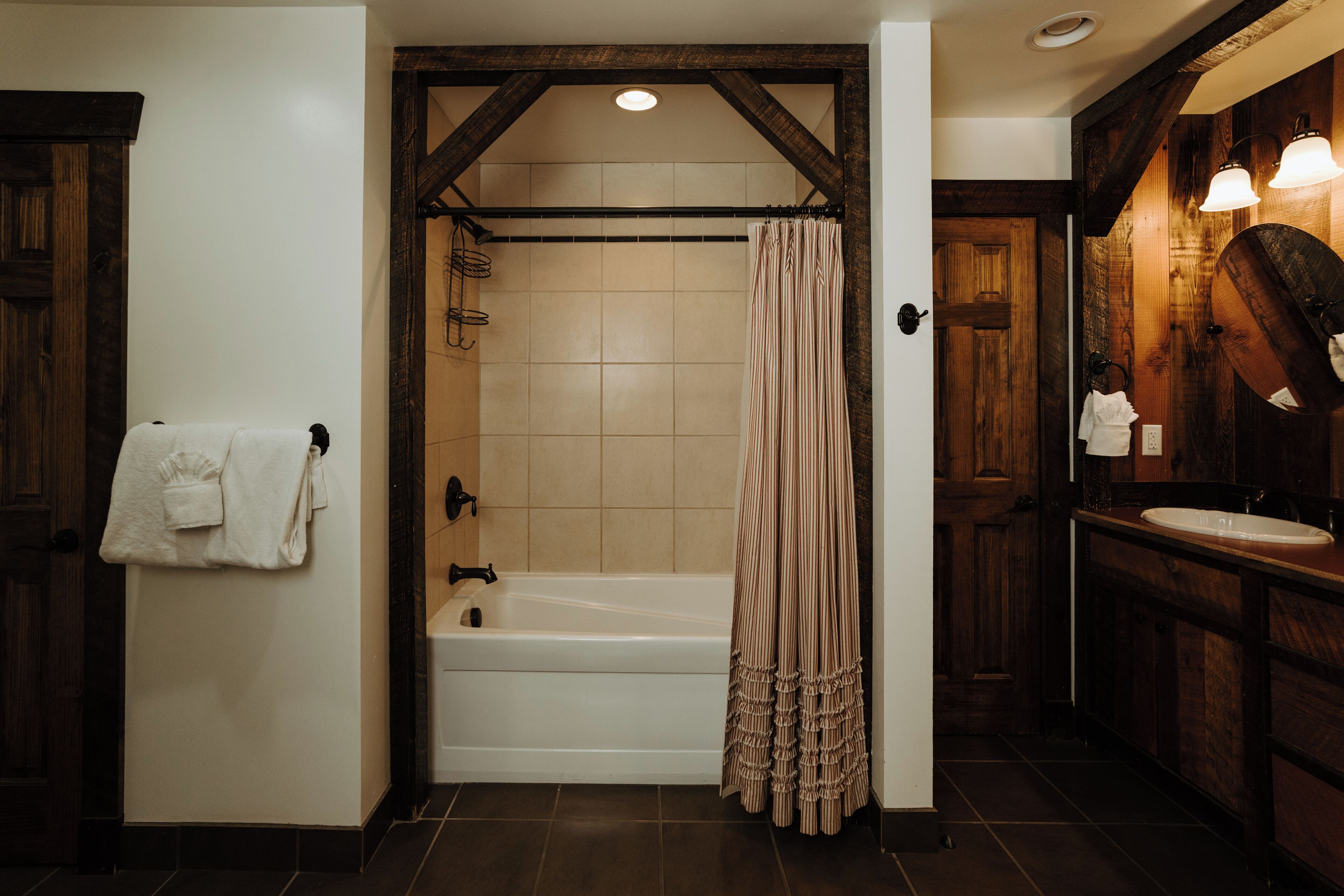 A bathroom with a bathtub, a shower curtain, a towel rack, and a wooden vanity with a mirror.