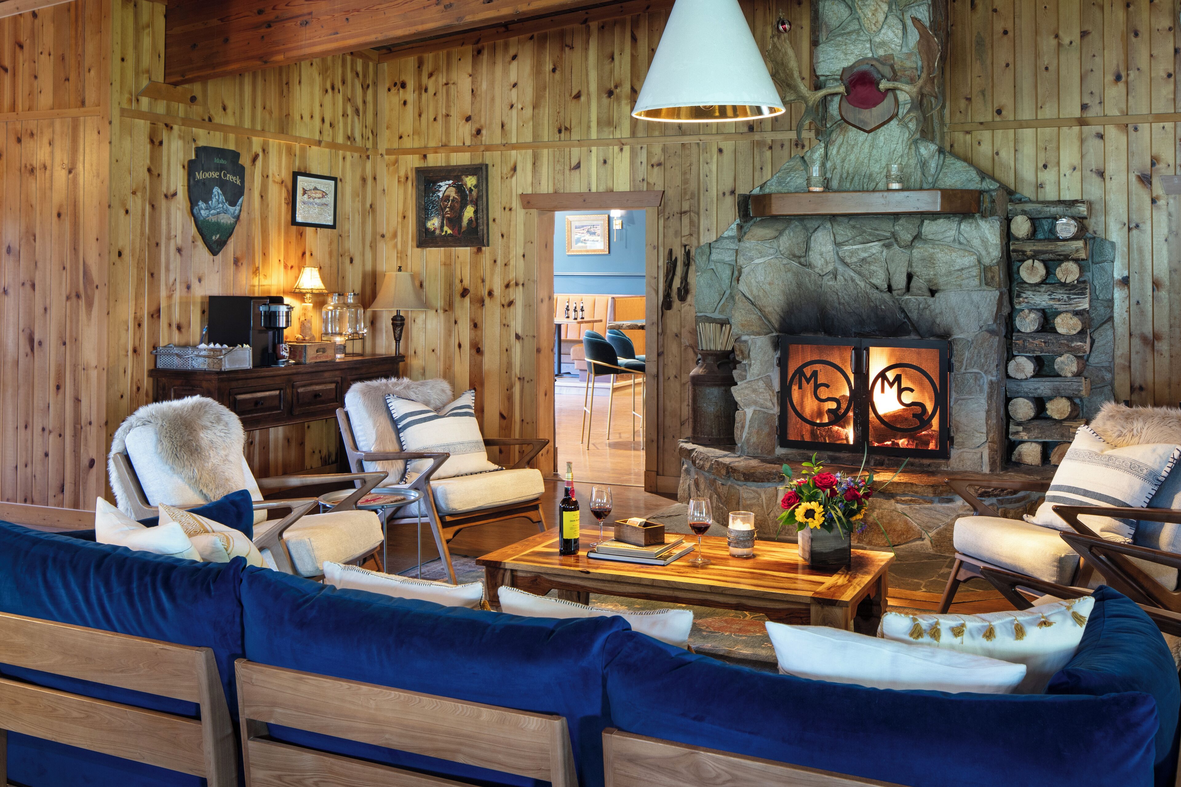 A cozy lodge interior with a stone fireplace, wooden walls, and comfortable seating.