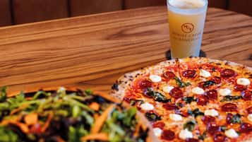 A pizza and a salad on a wooden table with a drink in the background.