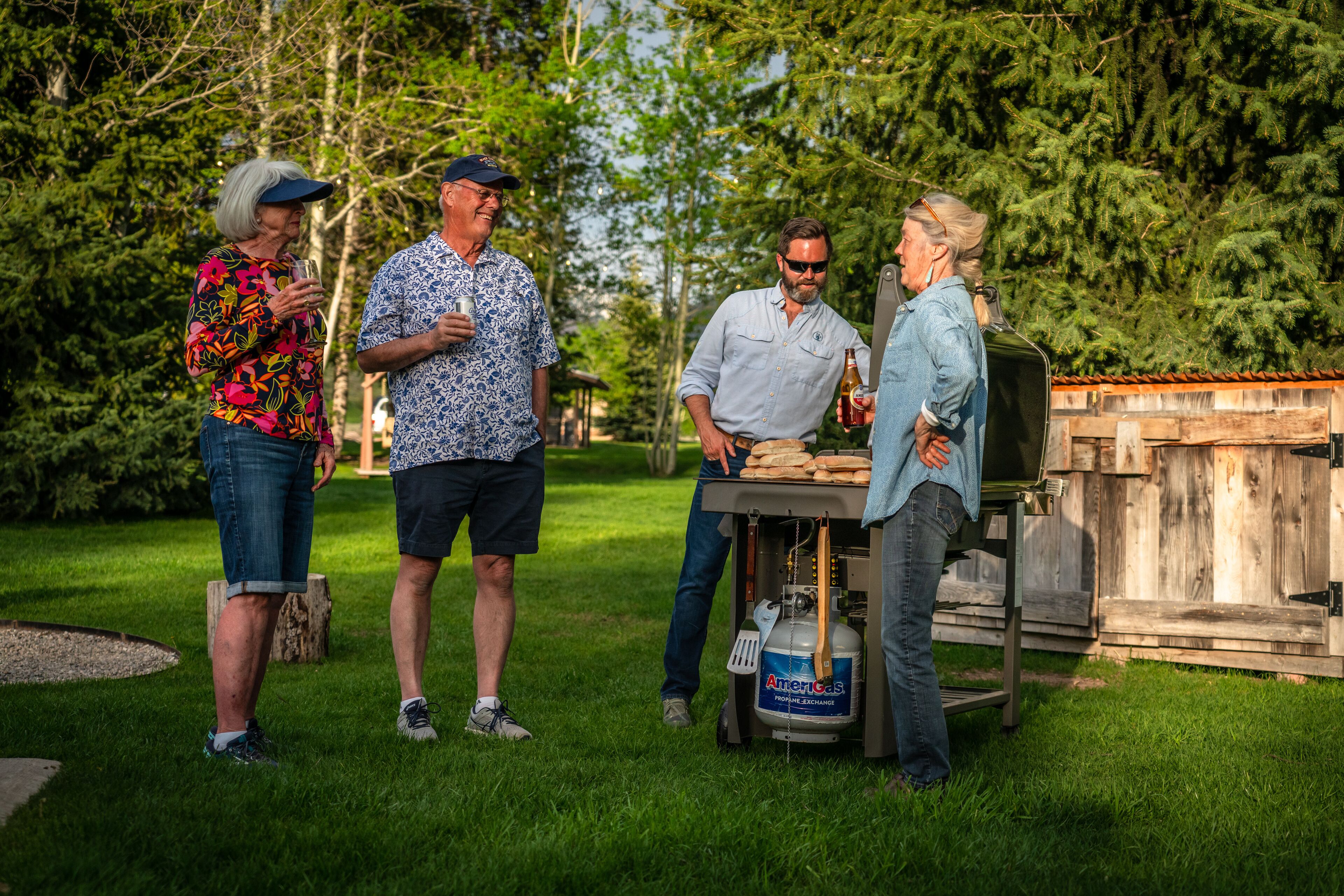 Un groupe de personnes se tient à l’extérieur, près d’un barbecue équipé d’une bouteille de propane.