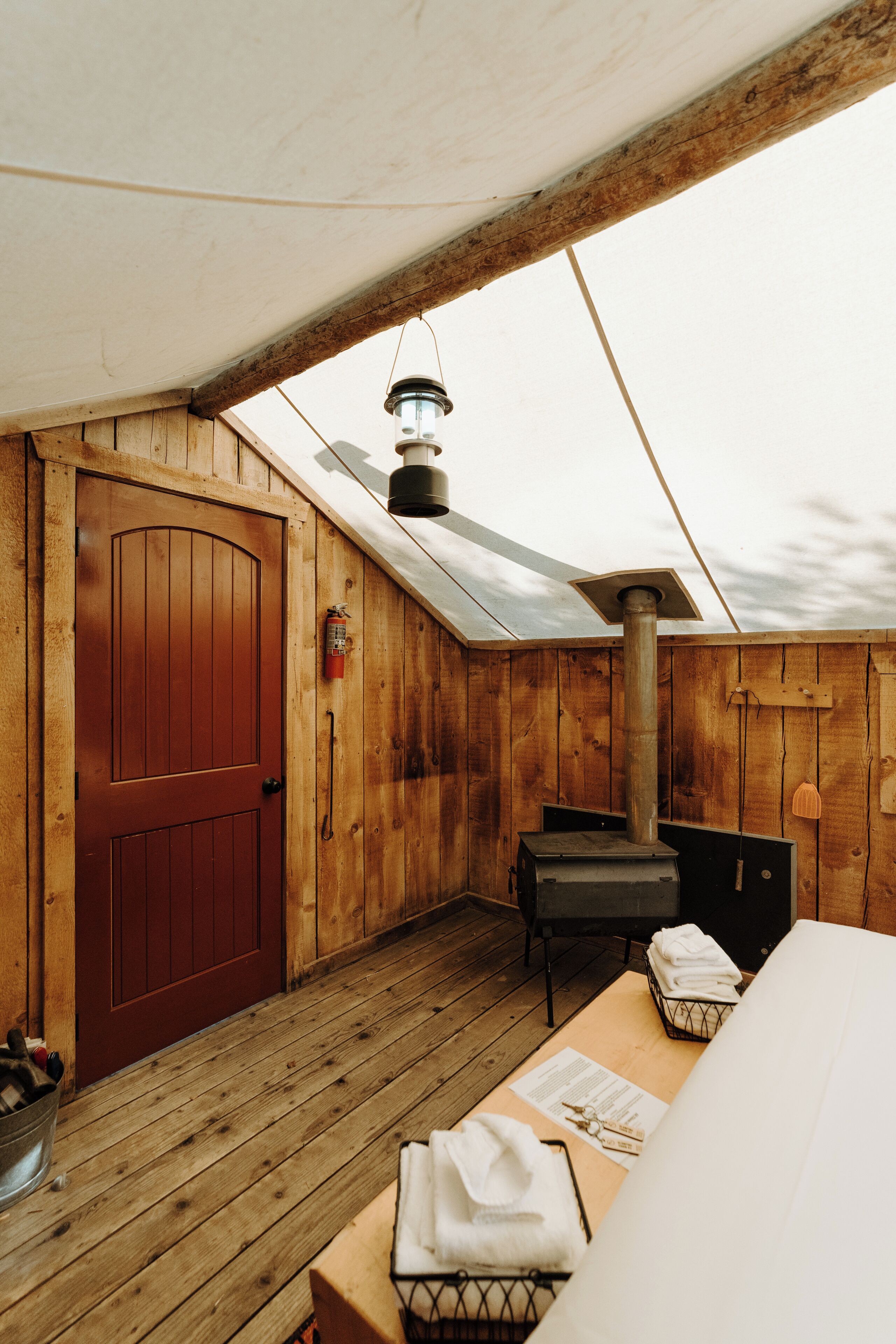 A wooden cabin with a red door, a table with towels, a chair, and a lantern on the roof.
