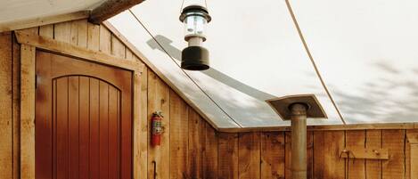 A wooden cabin with a red door, a table with towels, a chair, and a lantern on the roof.