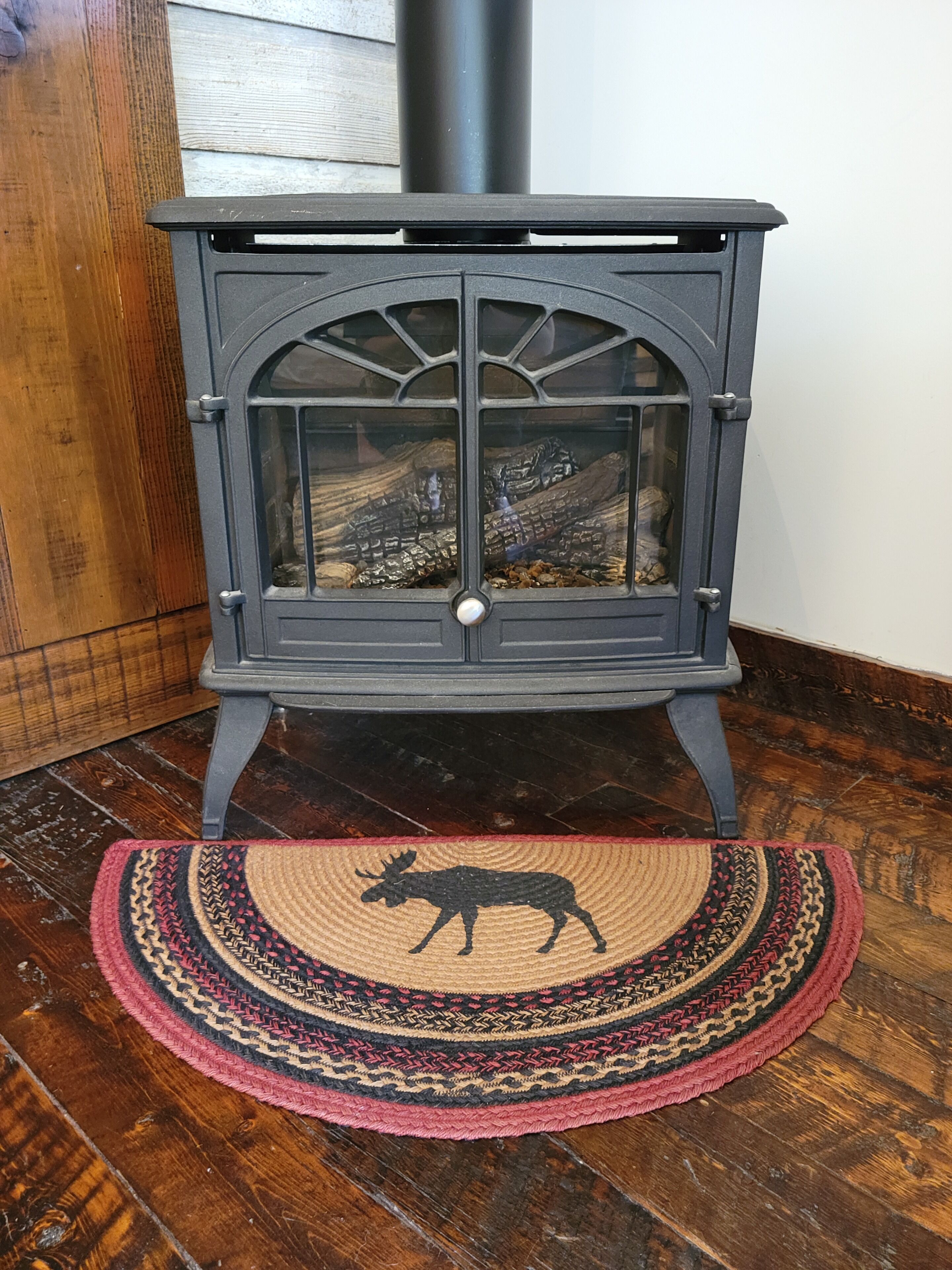 A wood-burning stove with a glass door, placed on a wooden floor with a decorative rug featuring a moose design.
