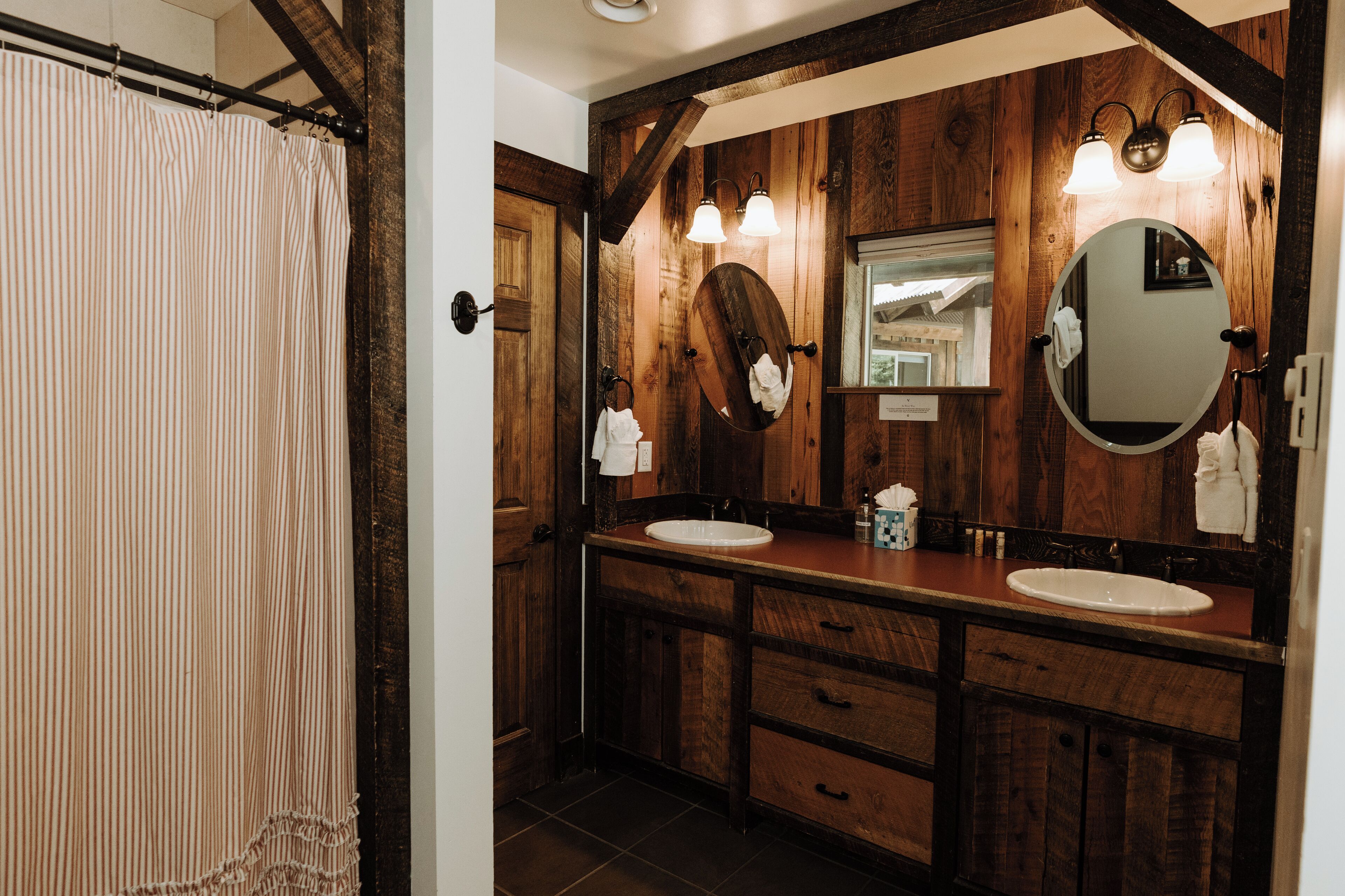 Un baño de madera con dos lavamanos, un espejo grande y una cortina de ducha.