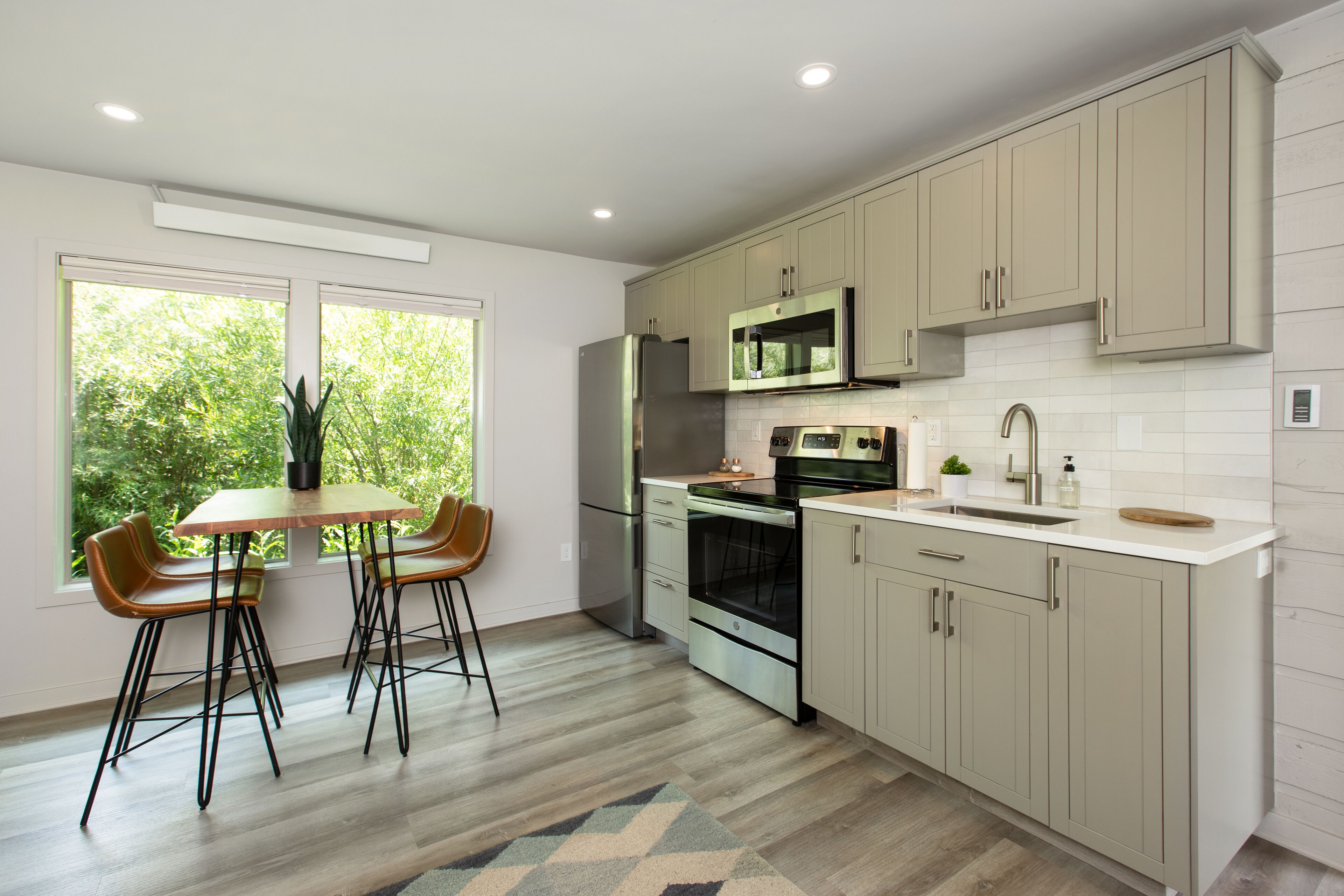 A modern kitchen with light wood cabinets, stainless steel appliances, and a dining area with two chairs.