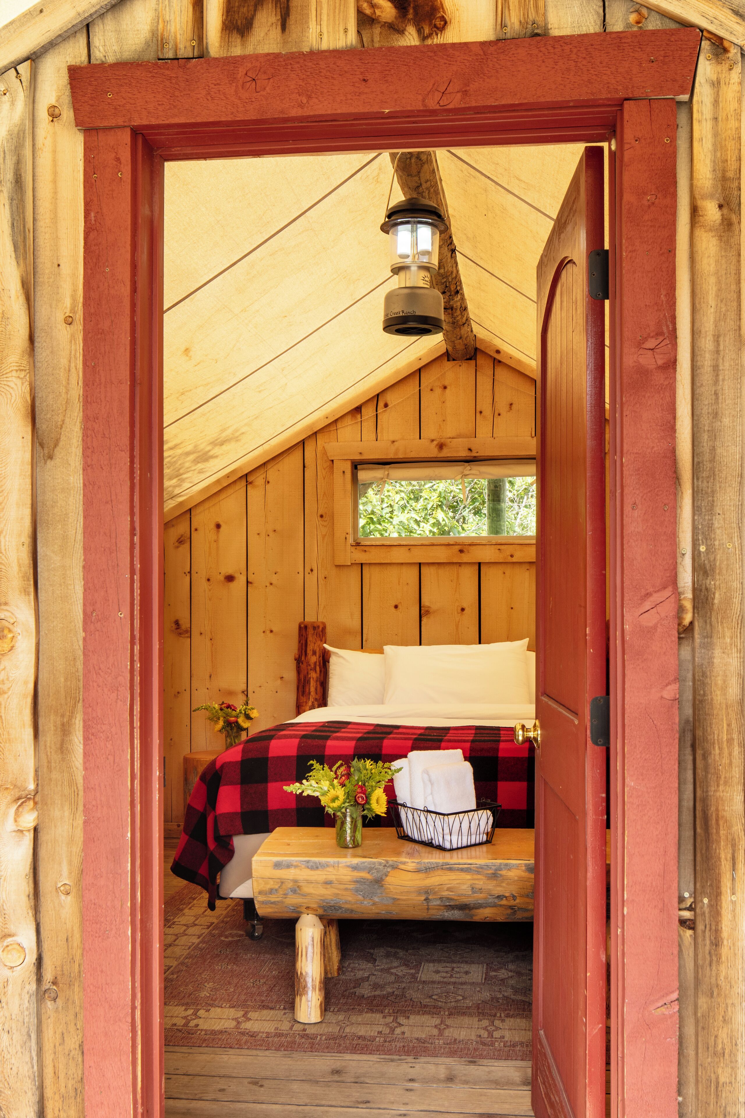 A cozy wooden room with a bed, a small table with a vase of flowers, and a window.