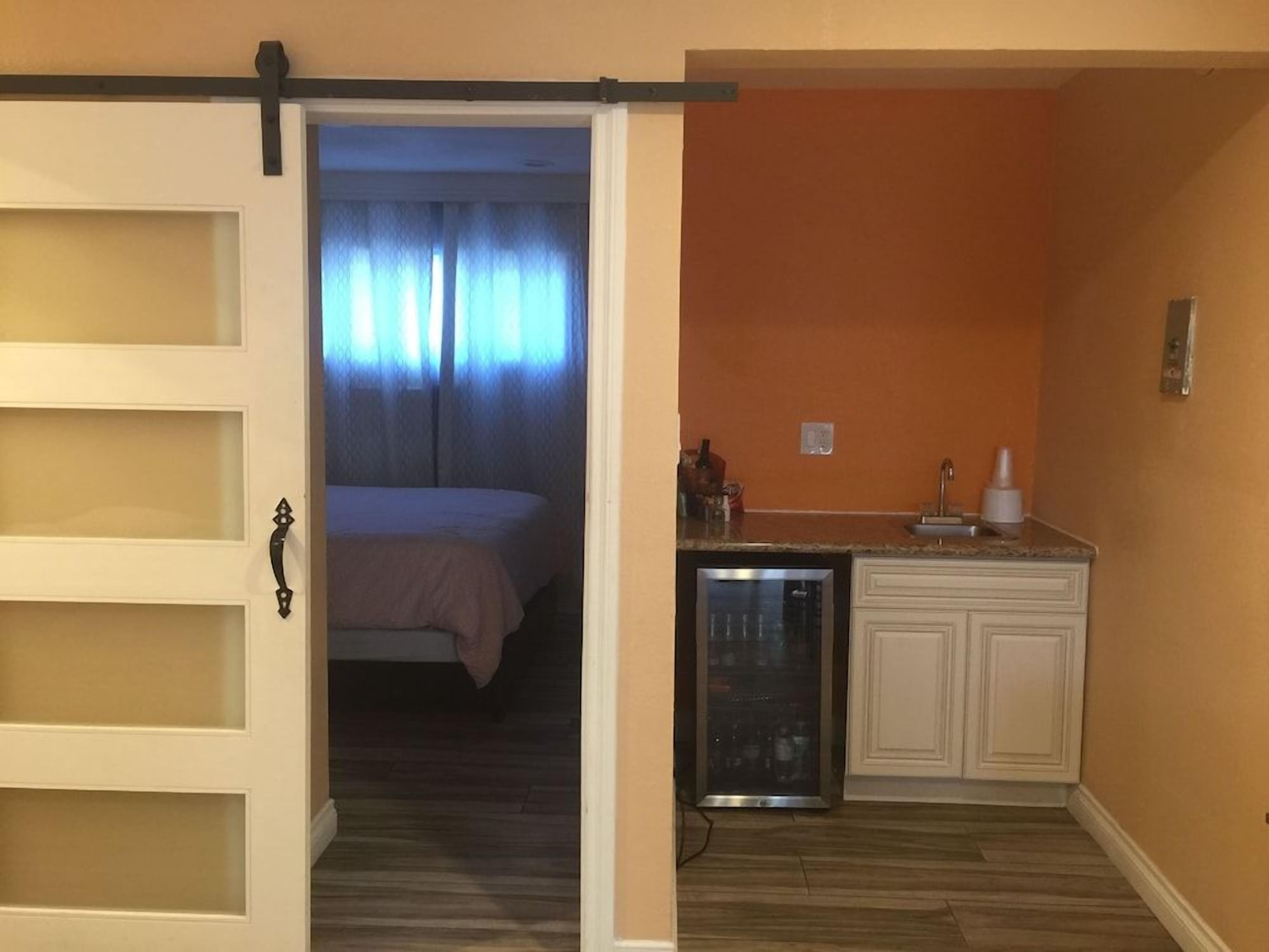 Una habitación con cama, una kitchenette equipada con refrigerador y una puerta corredera que da a otra habitación.