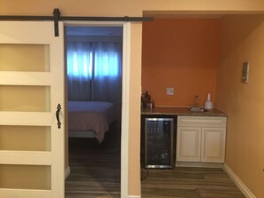 A room with a bed, a kitchenette with a refrigerator, and a sliding door leading to another room. - Tradewinds All Suite Hotel (Inglewood)