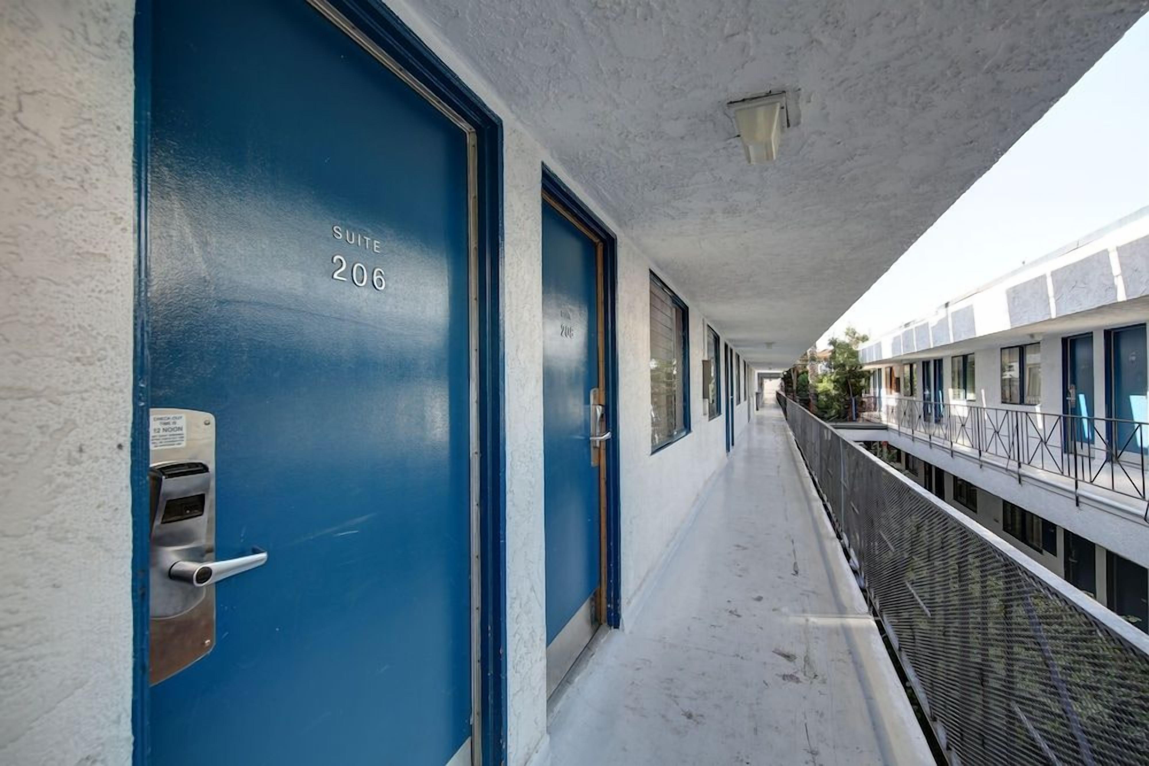 Un pasillo con puertas azules, cada una con el número de una suite, que conduce a un balcón con barandilla de metal.