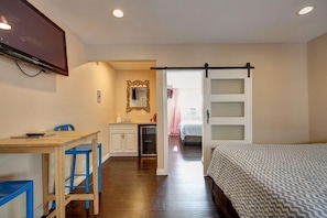 A bedroom with a bed, a desk with a chair, a mirror, and a sliding door leading to another room. - Tradewinds All Suite Hotel (Inglewood)