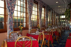 A restaurant with long tables, wooden chairs, and floral curtains. - Tradewinds All Suite Hotel (Inglewood)